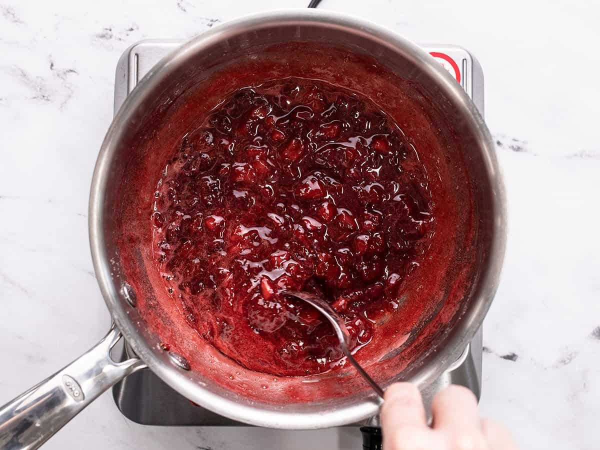 Strawberry syrup in a pot with a spoon in it.