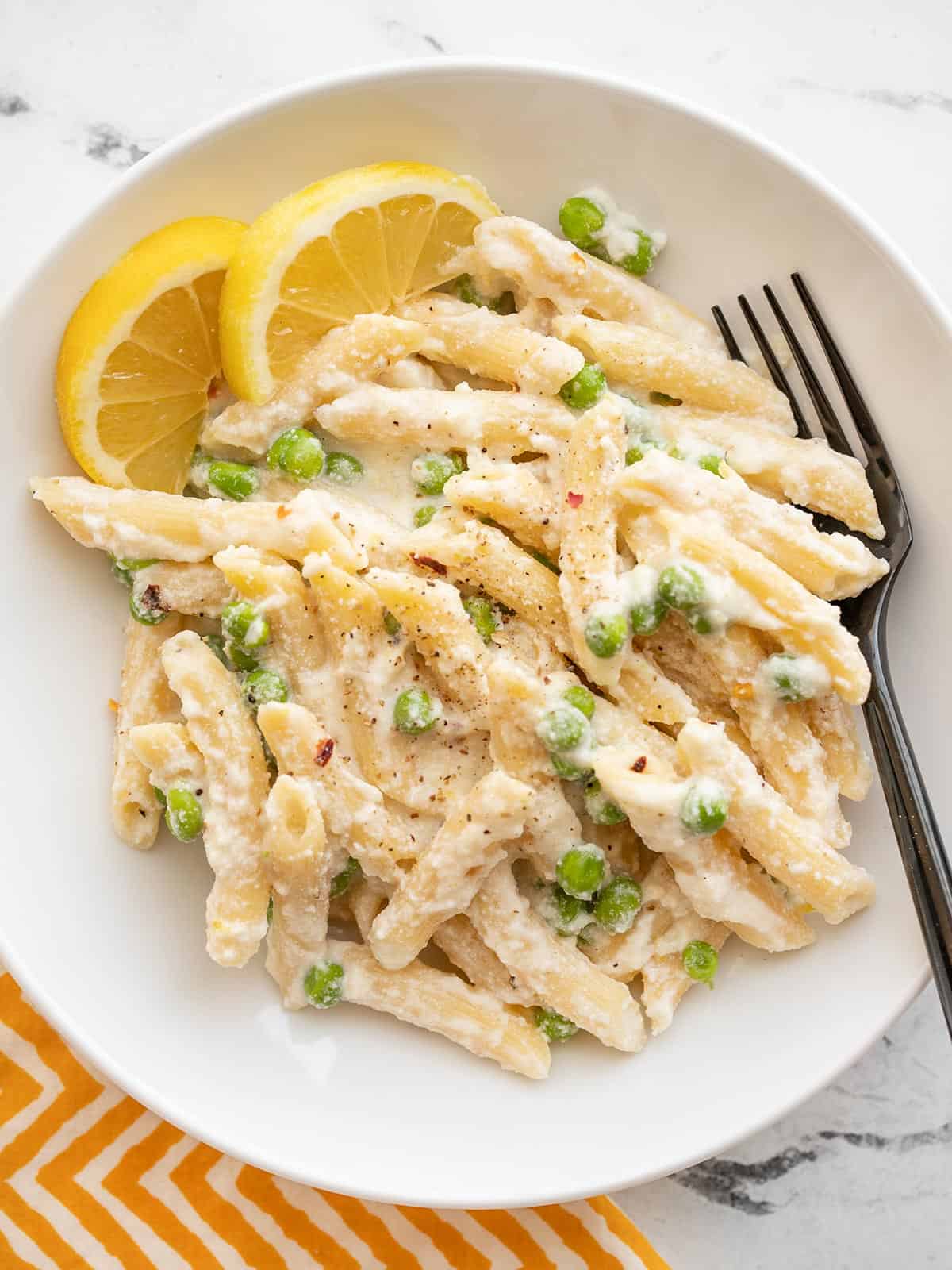 Overhead view of a bowl of lemon ricotta pasta with a fork and lemon wedges.