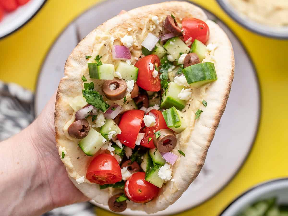 Close up of hand holding loaded hummus pita.