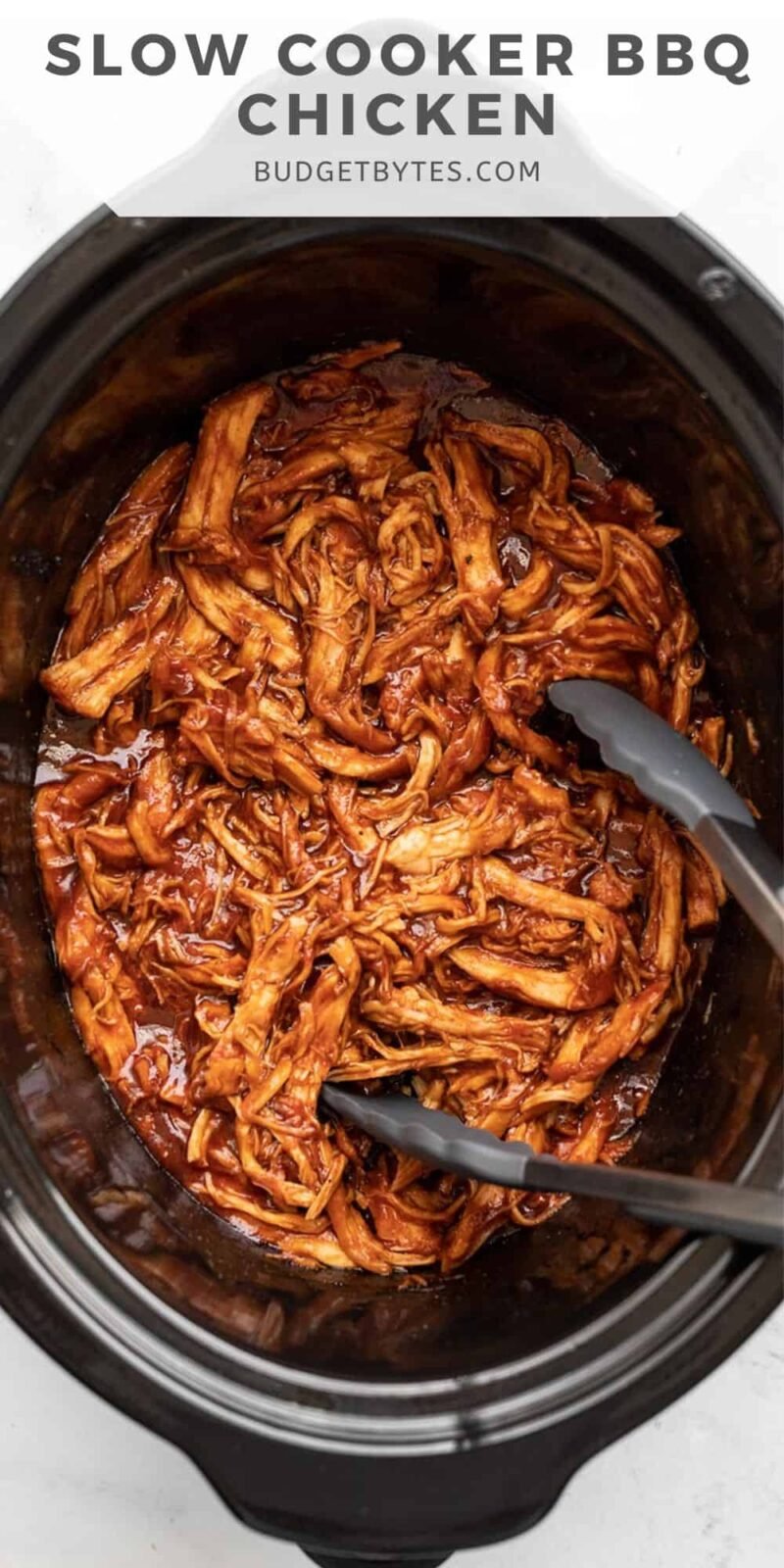 Overhead view of slow cooker bbq chicken in the slow cooker with tongs.