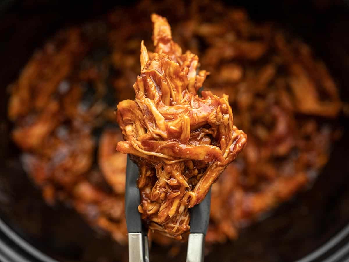 Close up of tongs holding pulled BBQ Chicken.