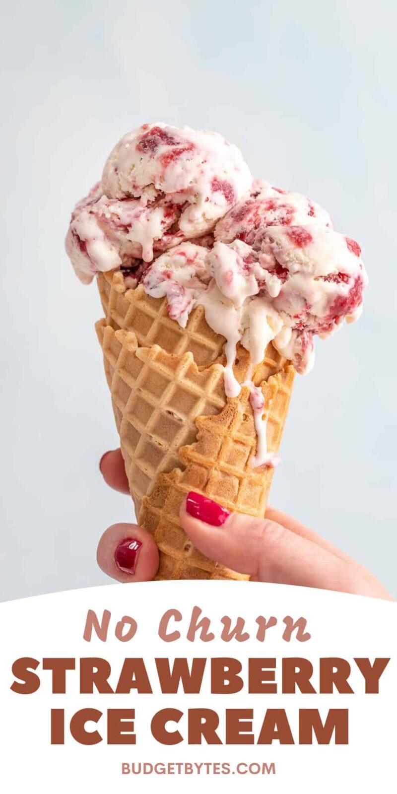 Side view of a hand holding a strawberry ice cream cone.