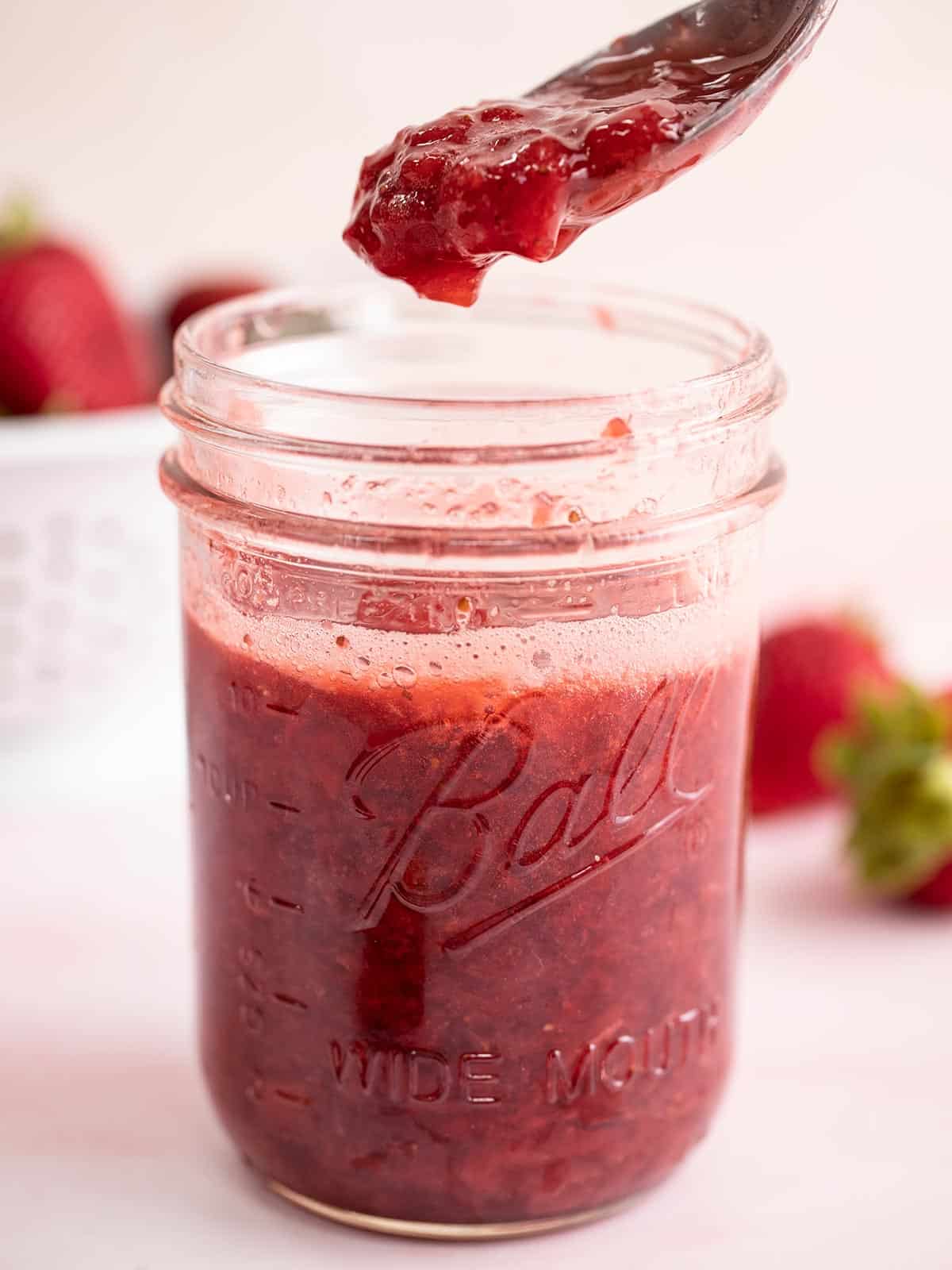 Finished strawberry syrup dripping off a spoon into a jar.