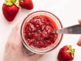 Overhead view of strawberry syrup in a jar with a spoon.