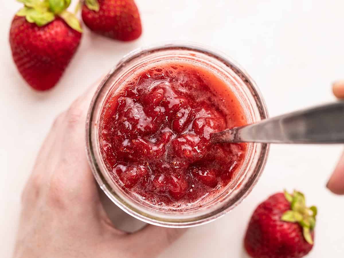 Overhead view of strawberry syrup in a jar with a spoon.