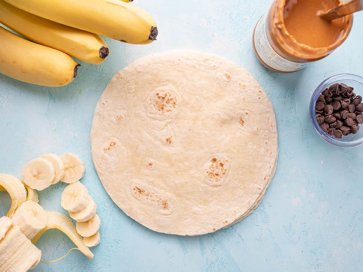 Tortilla surrounded by bananas, peanut butter, and chocolate chips.