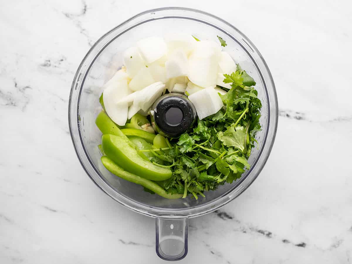 Overhead shot of cilantro, green bell pepper, yellow onion, and garlic in a food processor.