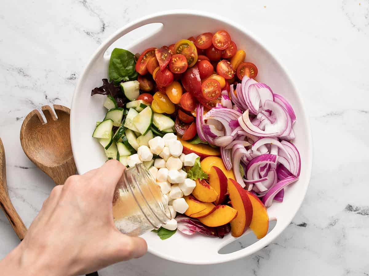 Overhead shot of panzanella salad being dressed in a white bowl with wood serving spoons next to it.