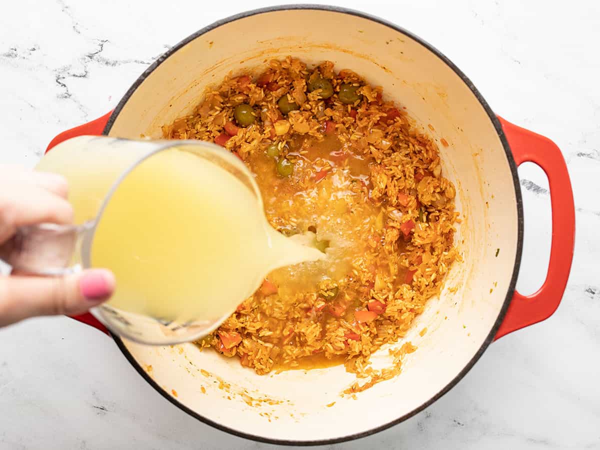 Adding chicken stock to ingredients in a red Dutch oven.