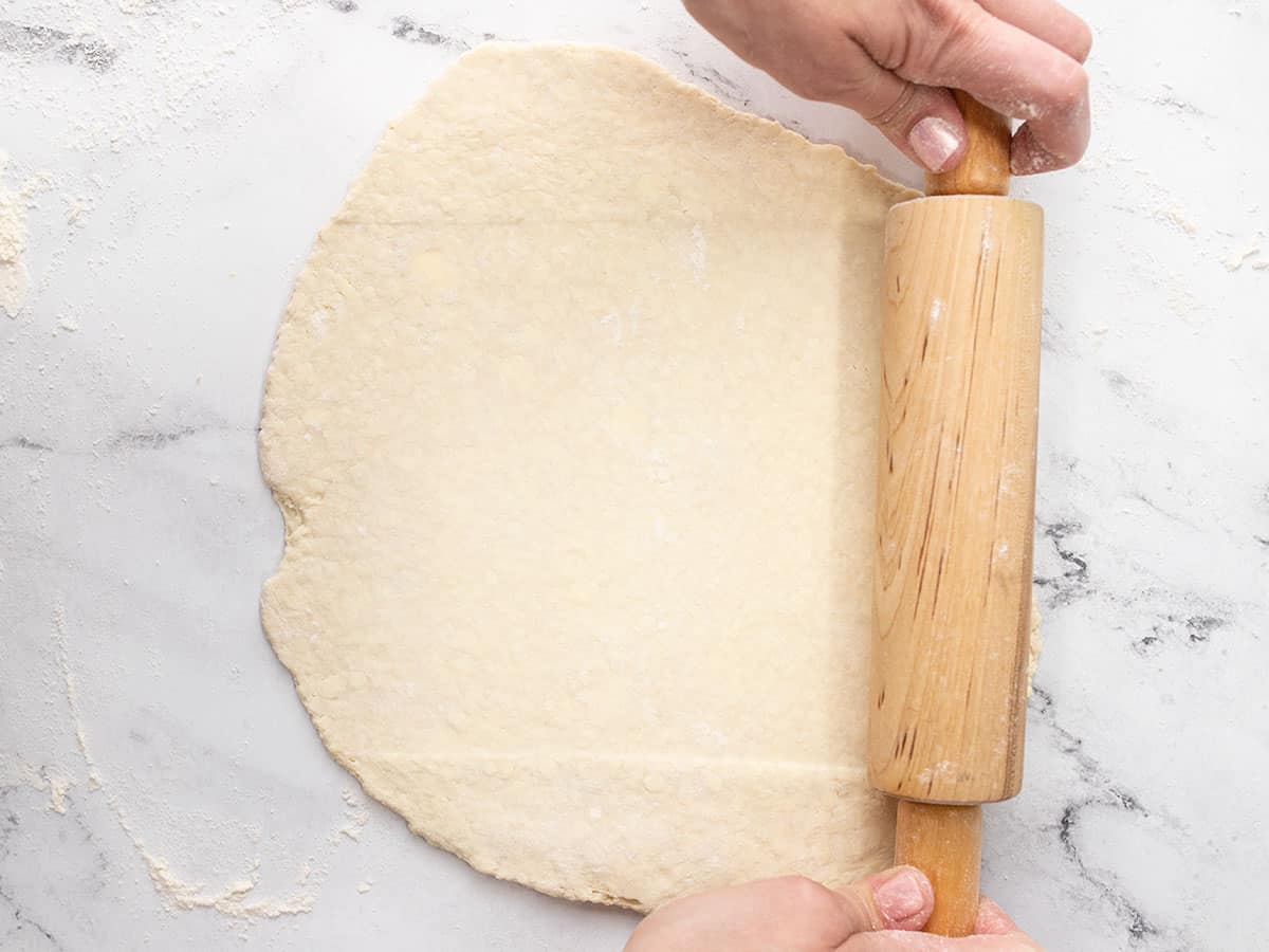 Overhead shpt pf pie dough being rolled out by hand.