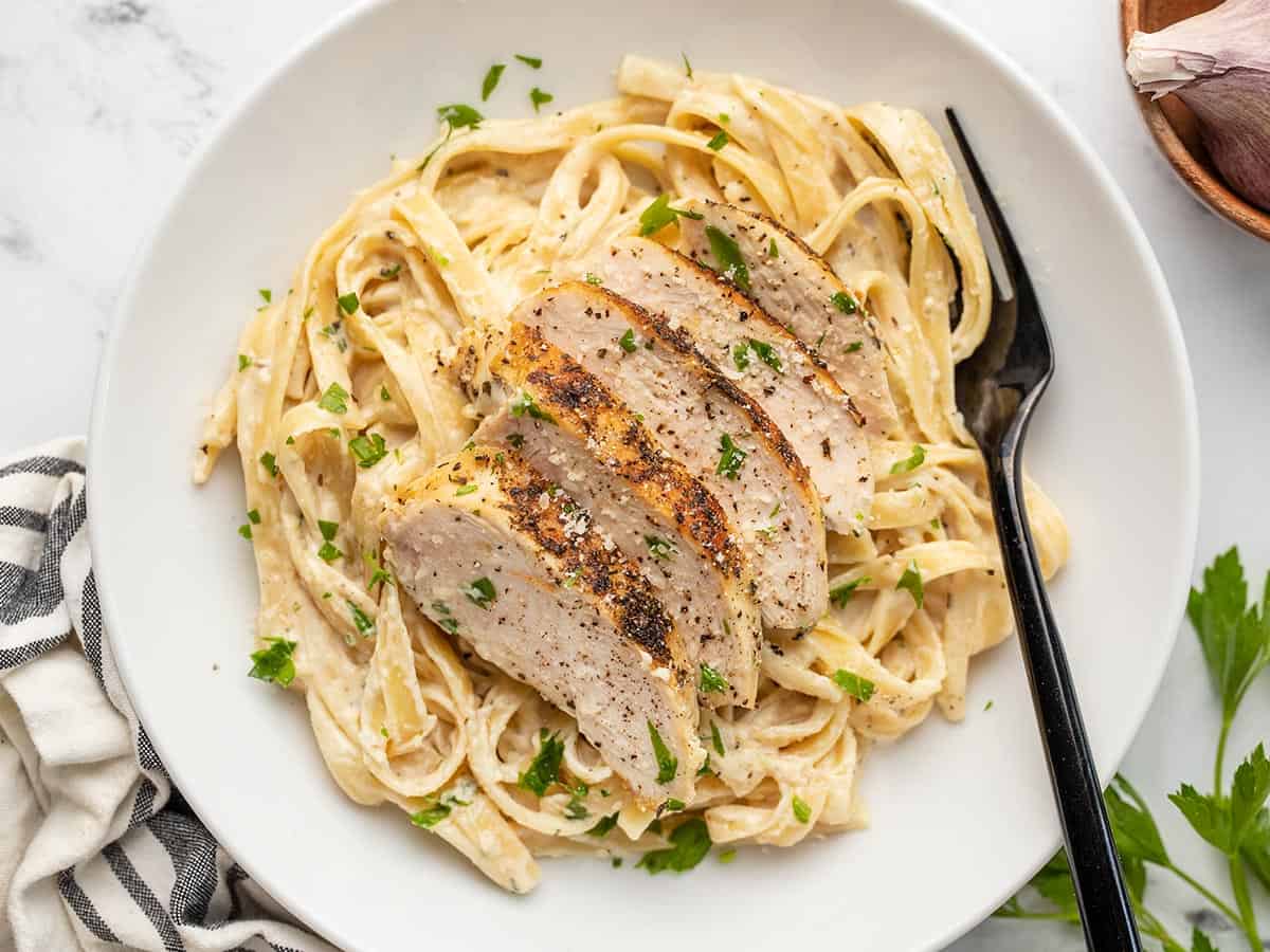 Overhead view of chicken alfredo in a shallow bowl with a fork.