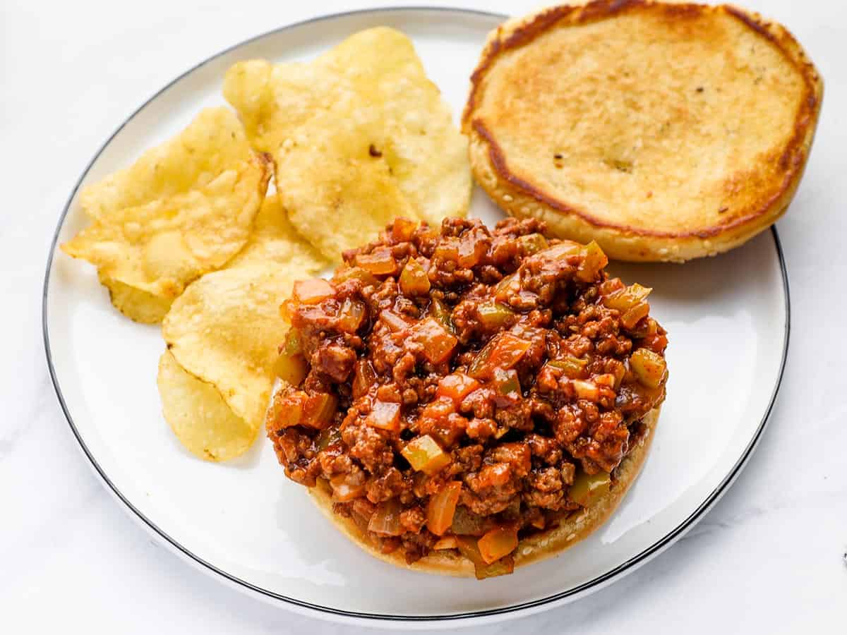 An open-faced sloppy joe on a plate with potato chips.