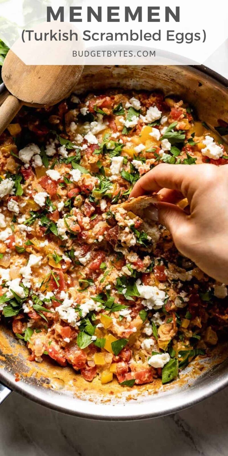 A hand dipping bread into a skillet full of Menemen.