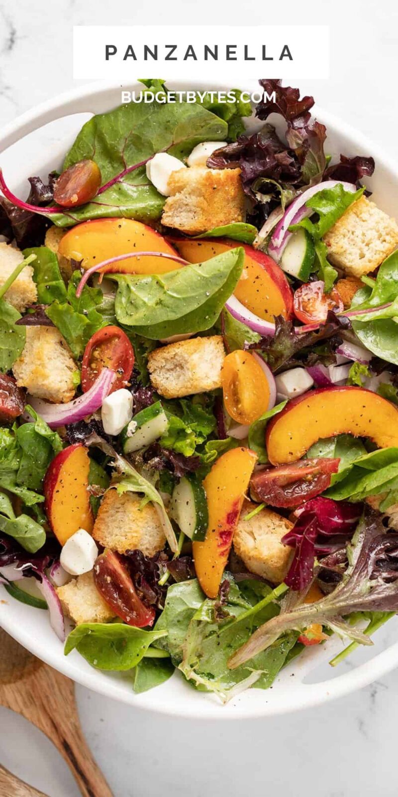 Overhead shot of panzanella salad in a white bowl with wood serving spoons next to it.