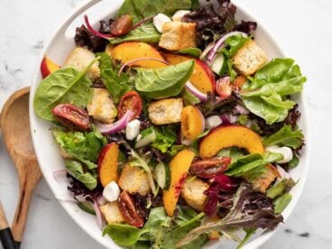 Overhead shot of panzanella salad in a white bowl with wood serving spoons next to it.