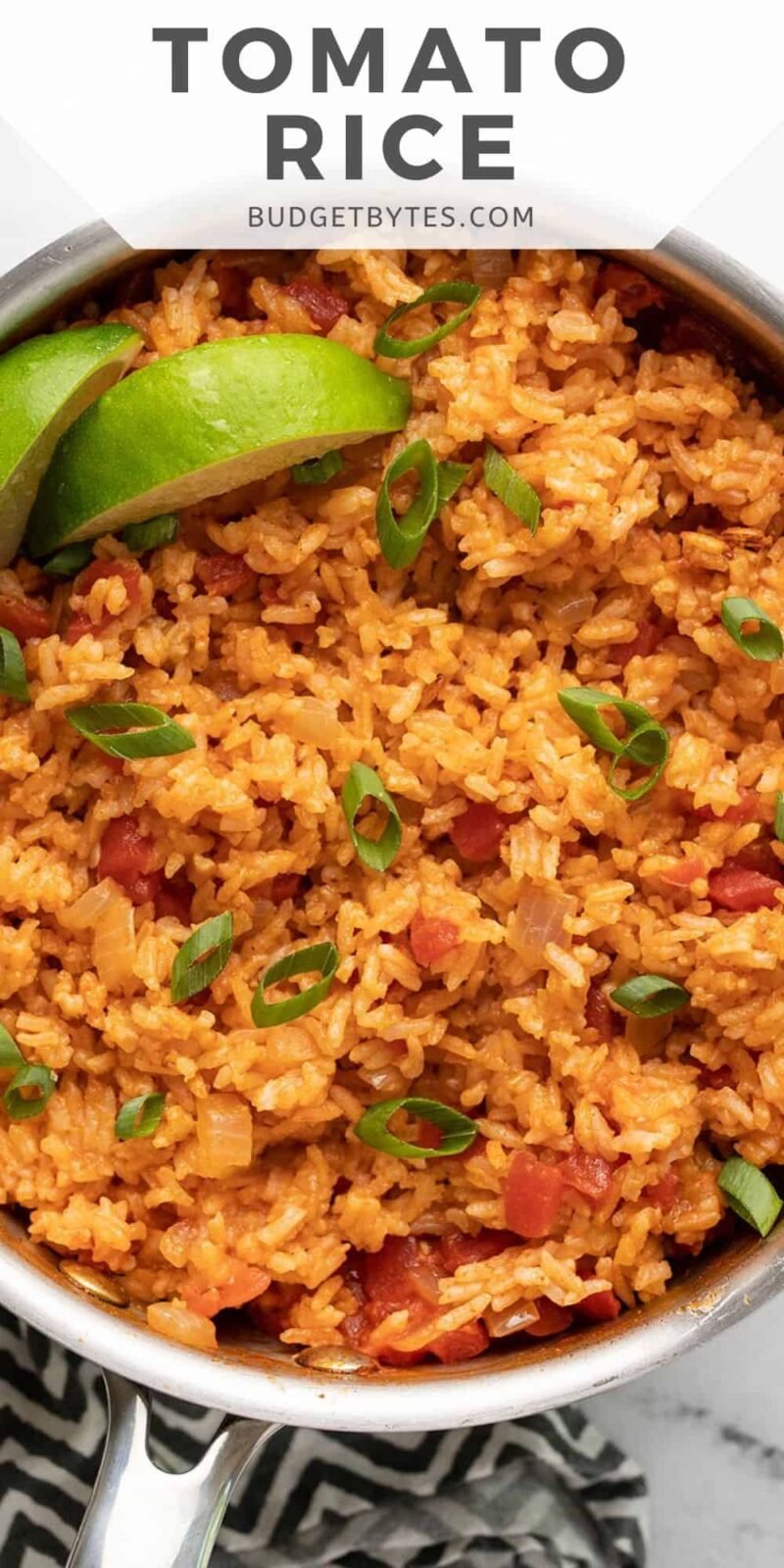 Overhead view of a pot full of tomato rice with lime and green onion.