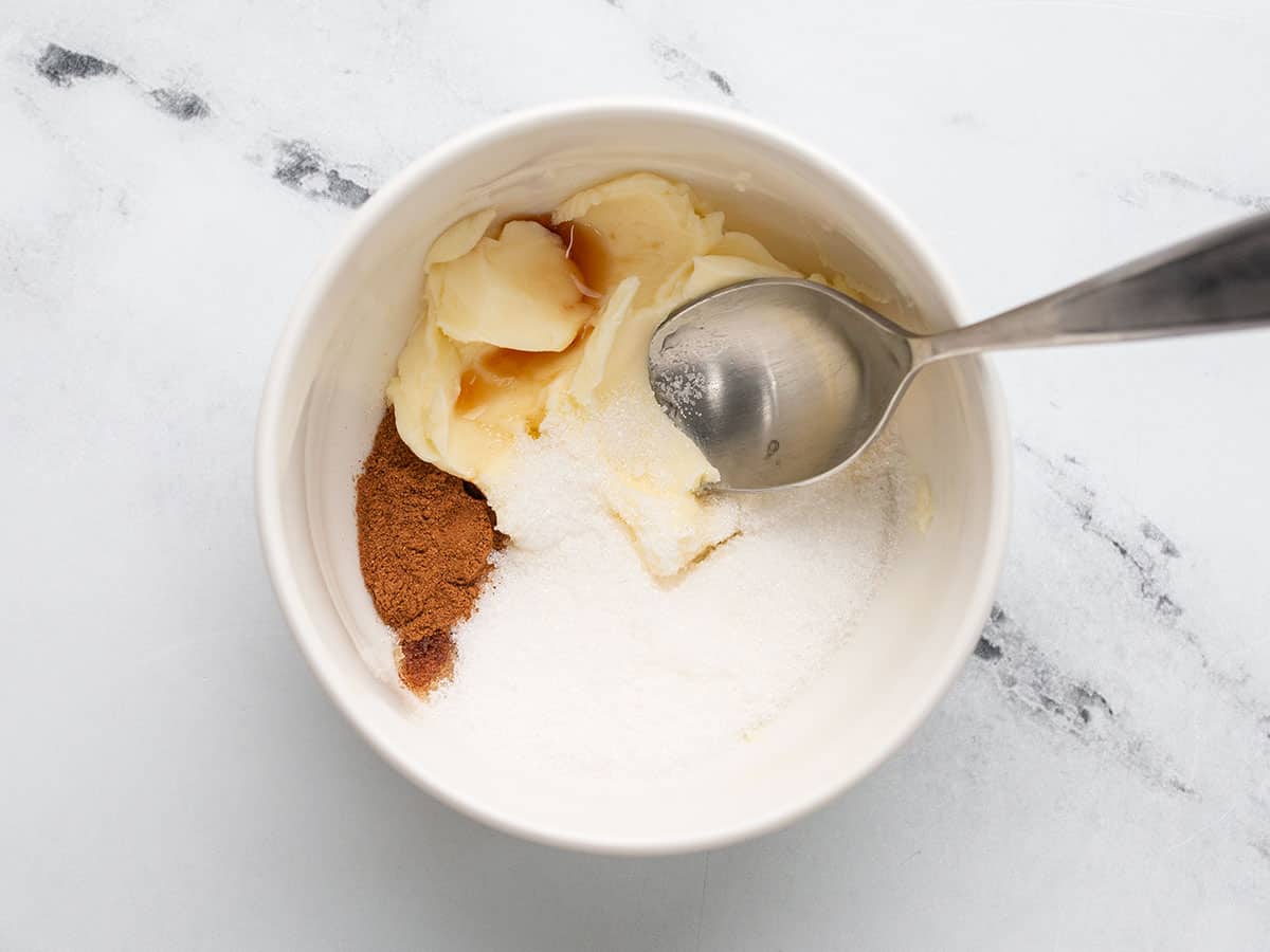 Overhead shot of cinnamon, butter, and sugar in a small bowl with a spoon in it.