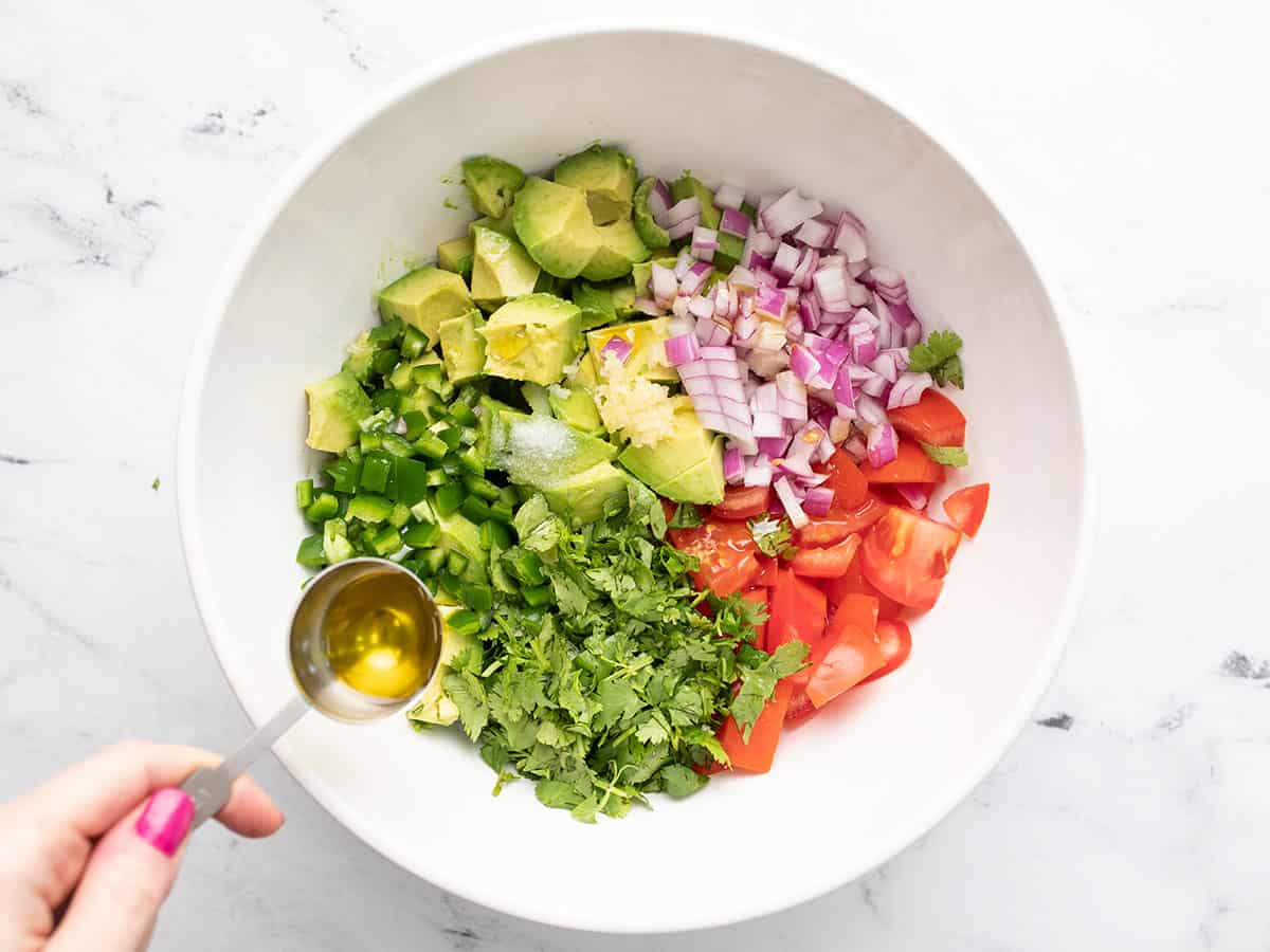 Prepped salad ingredients in the bowl, oil being drizzled over top.