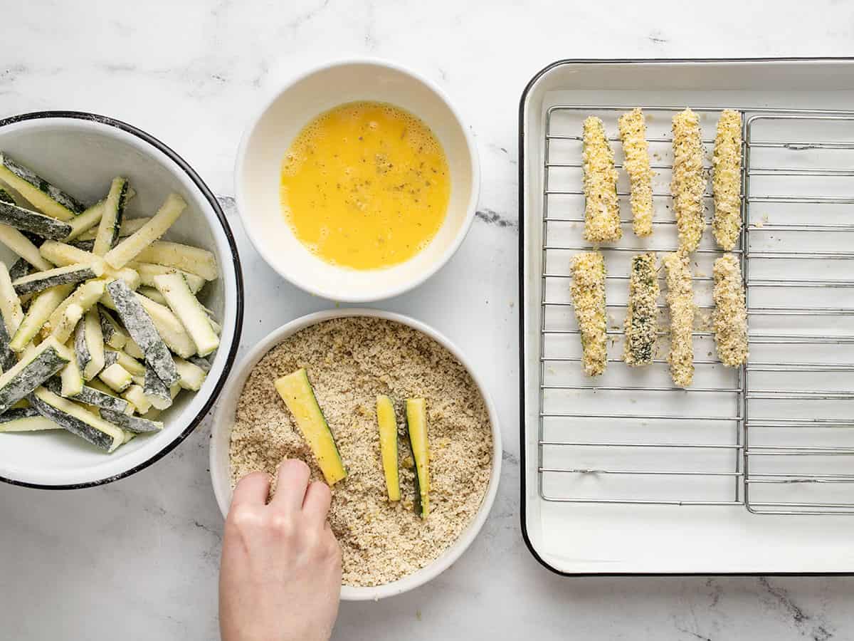 Zucchini being breaded and placed on a baking sheet.