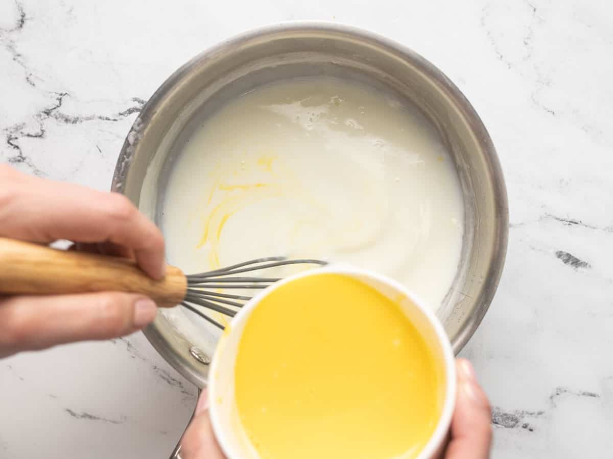 Overhead shot of tempered egg yolks being stirred into pudding in a pot.