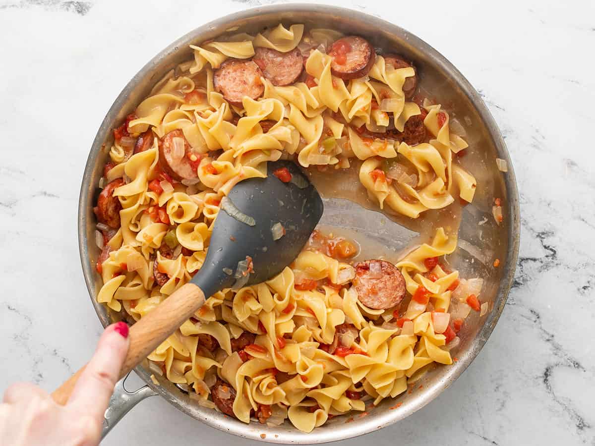 Cooked pasta pushed to the side of the skillet with the spatula.