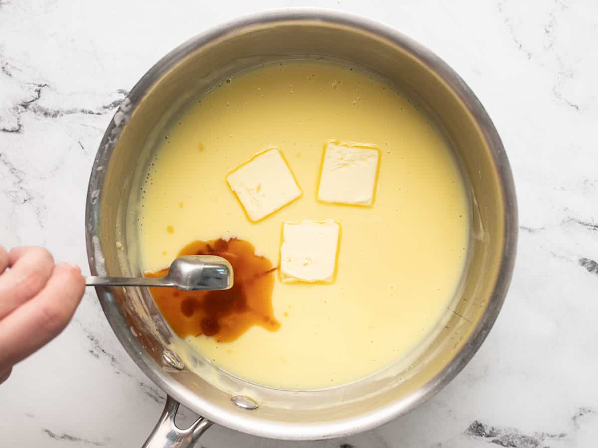 Overhead shot of vanilla and butter being stirred into pudding in a pot.