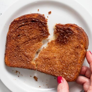 Overhead shot of hand holding cinnamon toast over a white plate.