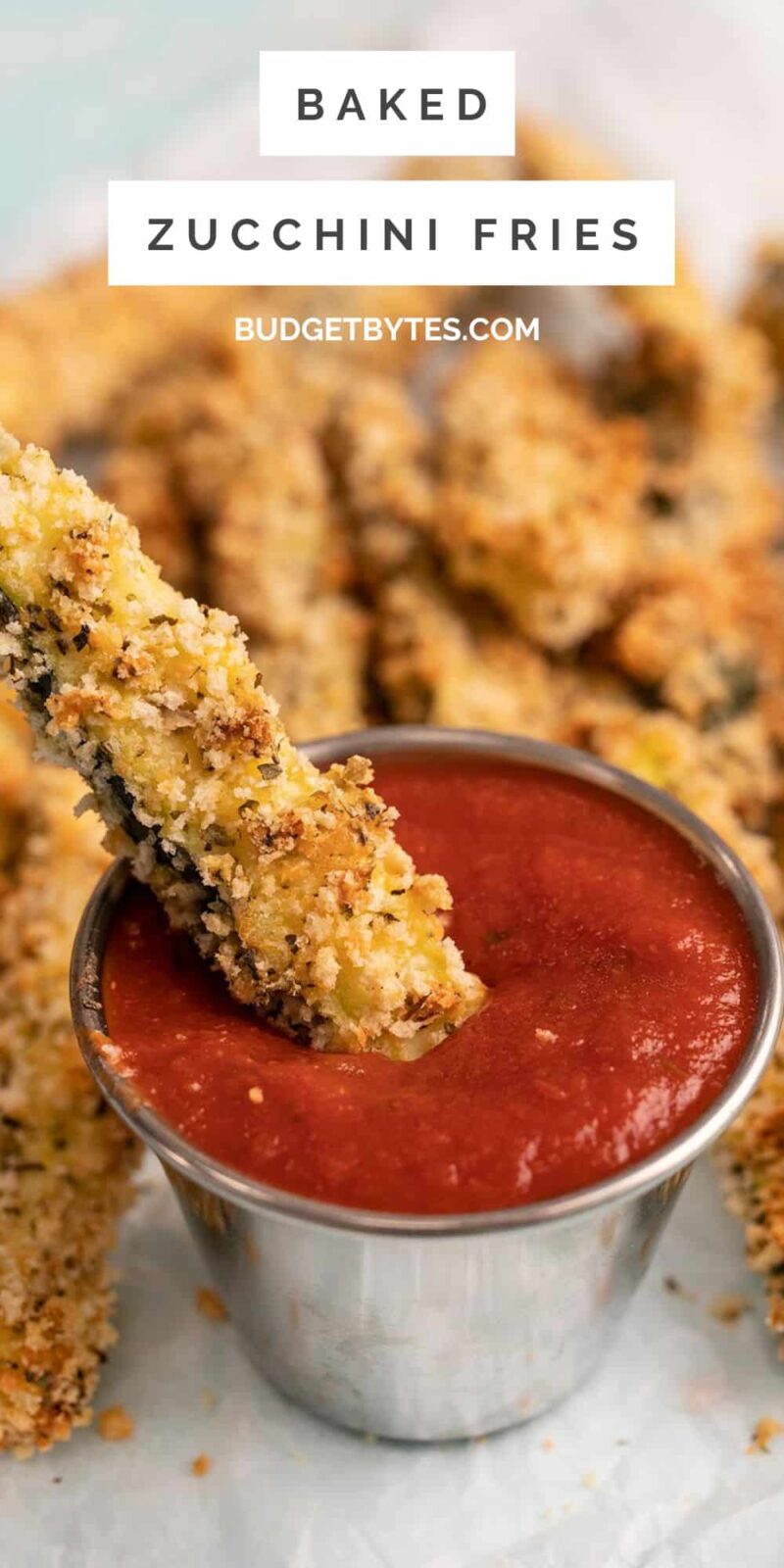 A baked zucchini fry dipped into a dish of pizza sauce.