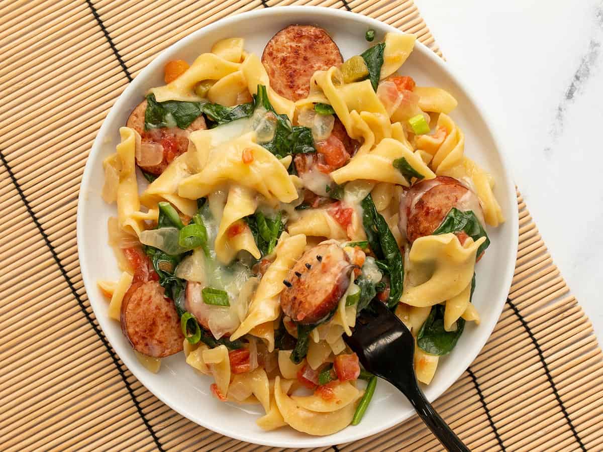 Cheesy sausage pasta on a plate with a black fork, on a bamboo mat. 