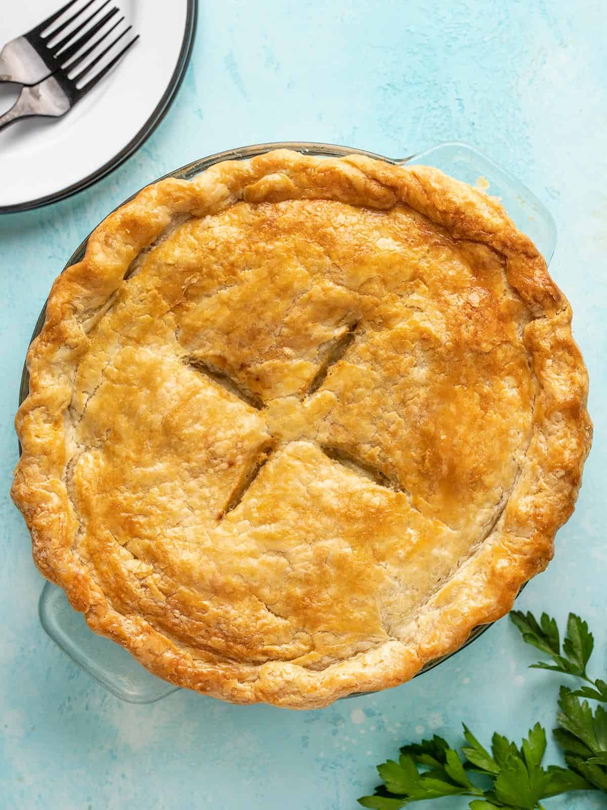 Chicken pot pie on a blue background with plates and parsley on the sides.