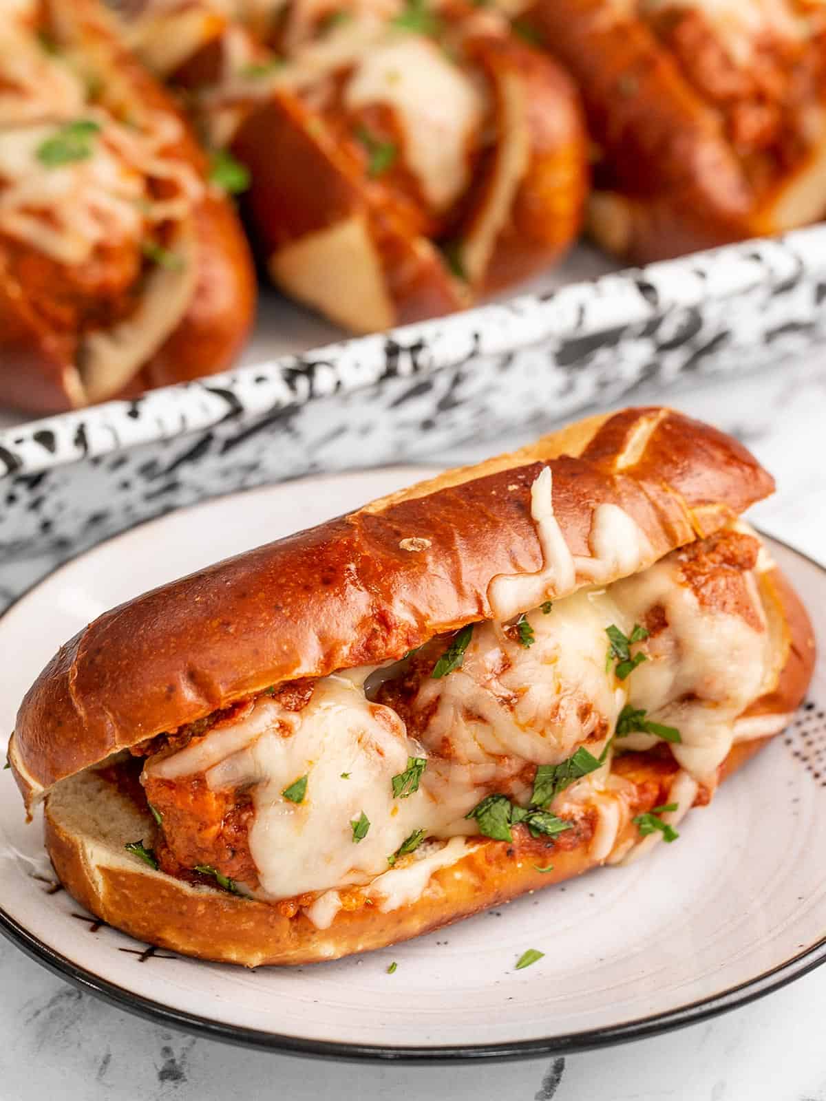 Side view of a meatball sub on a plate with the baking dish in the back.