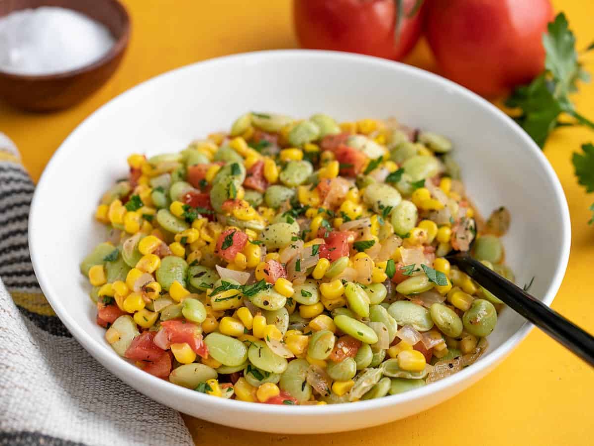 Side view of a bowl of succotash with a spoon.