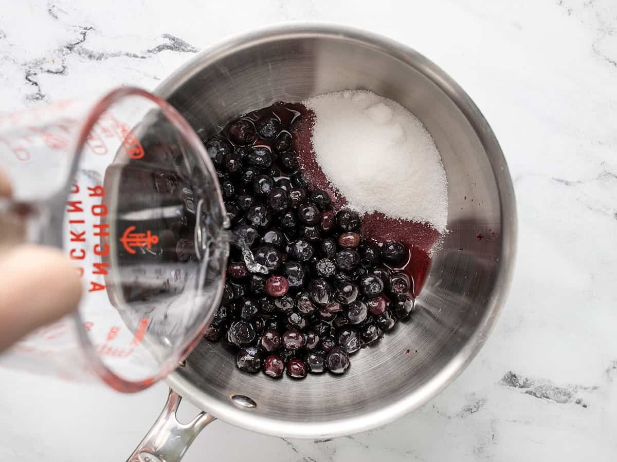 Overhead shot of sugar and water being added to blueberries.