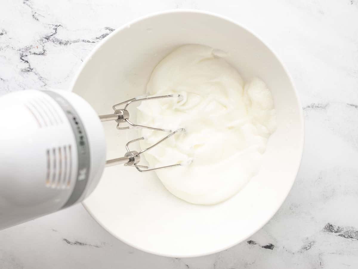 Overhead shot of hand mixer whipping egg whites in a white bowl.