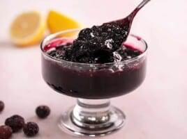 Side shot of blueberry sauce in a serving bowl with spoon in it.