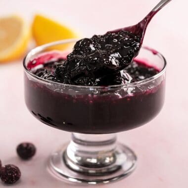 Side shot of blueberry sauce in a serving bowl with spoon in it.