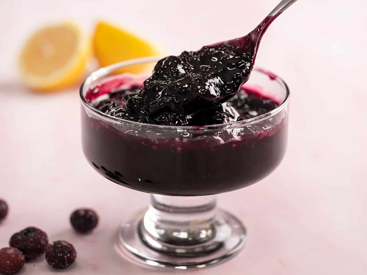 Side shot of blueberry sauce in a serving bowl with spoon in it.