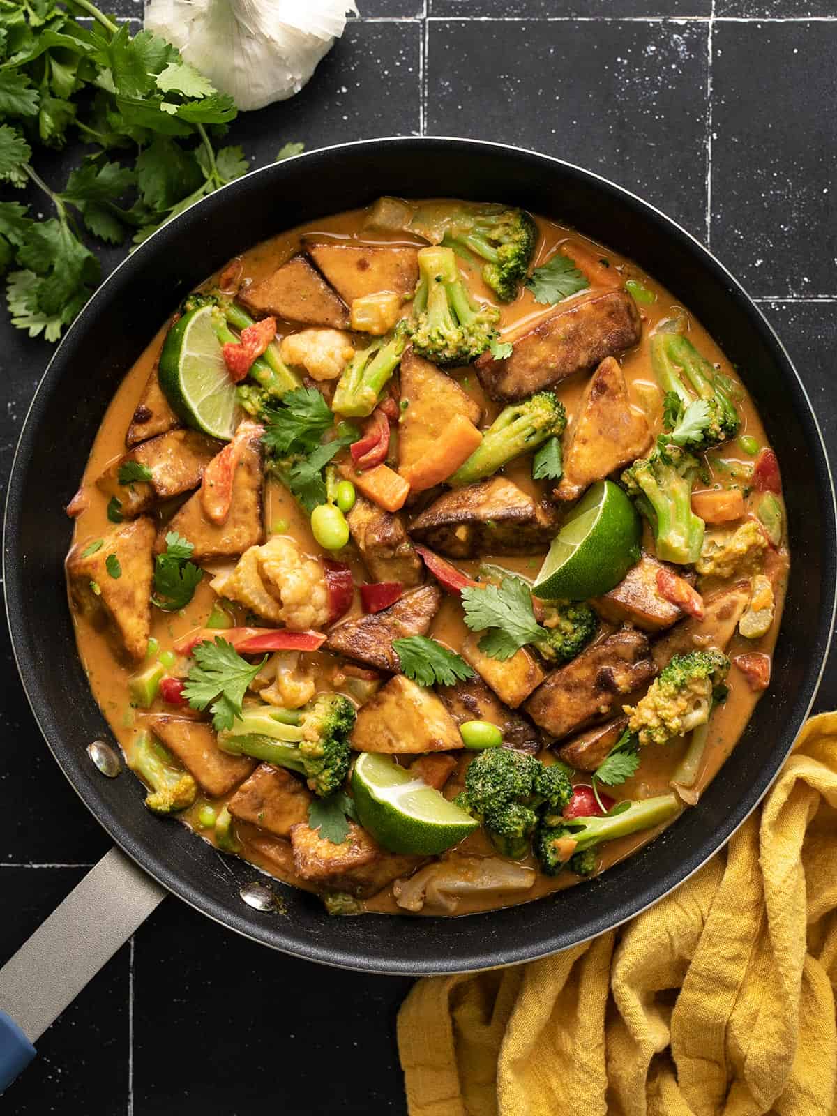 Overhead view of peanut tofu in a skillet on a black tile surface.