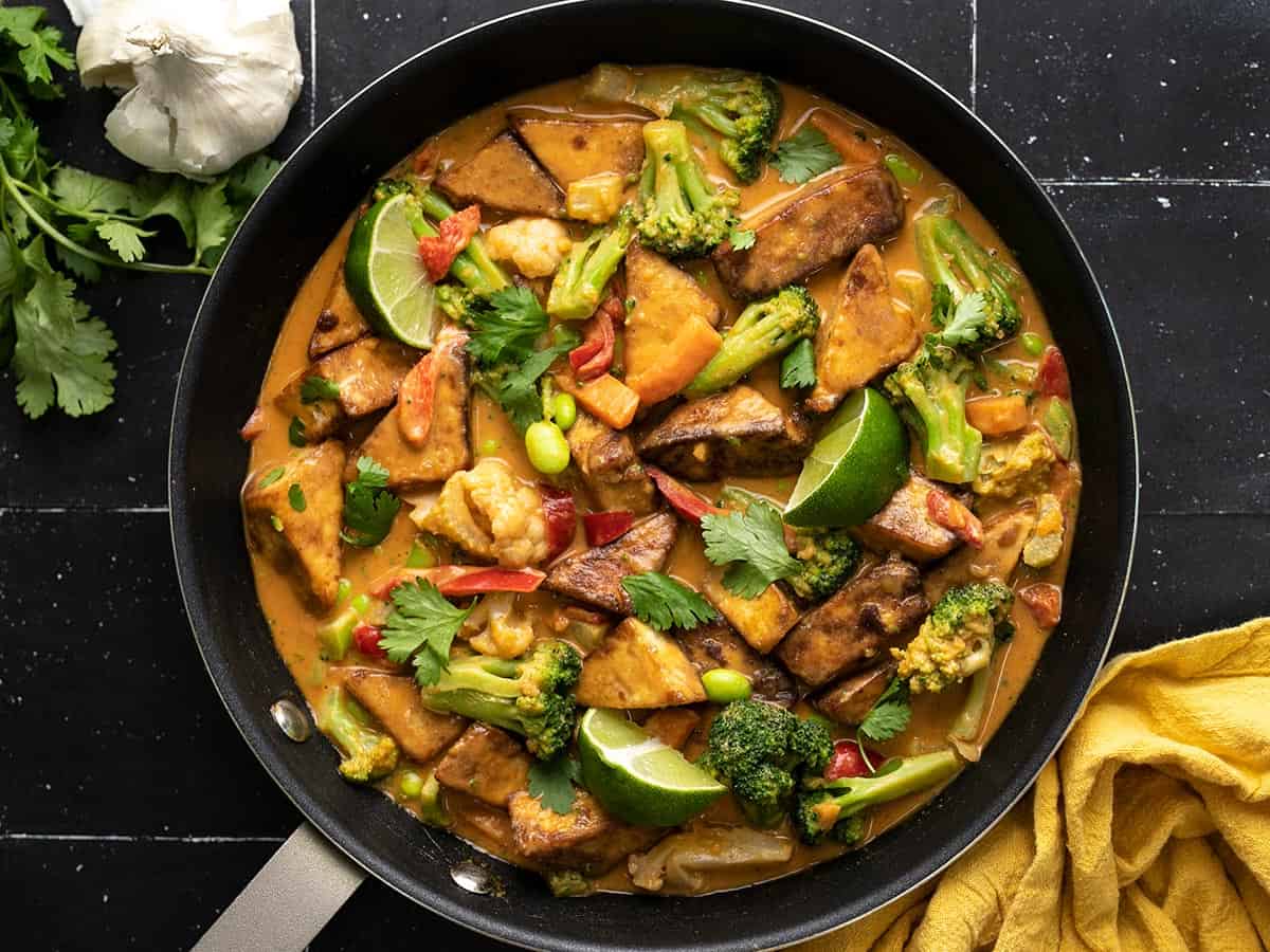 Overhead view of a skillet full of peanut tofu with limes and cilantro.