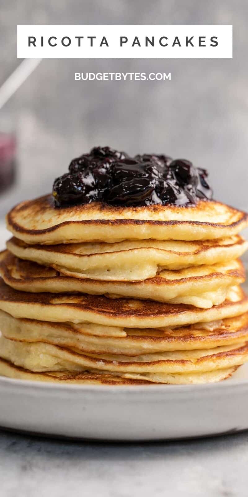 Side shot of a stack of ricotta pancakes with blueberry sauce on top.