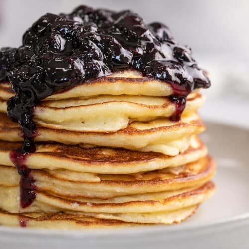 Side shot of a stack of ricotta pancakes with blueberry sauce on top.