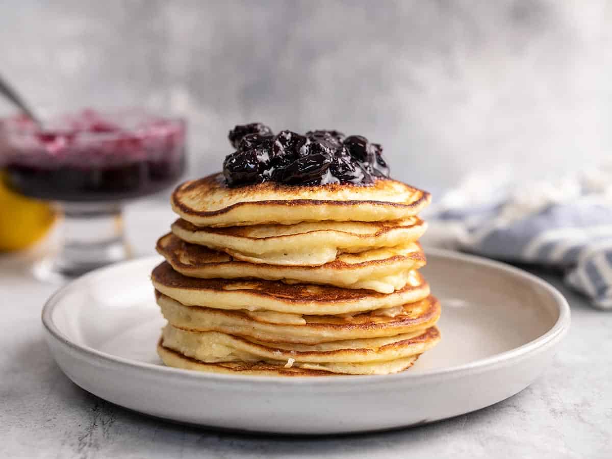 Side shot of a stack of ricotta pancakes with blueberry sauce on top.