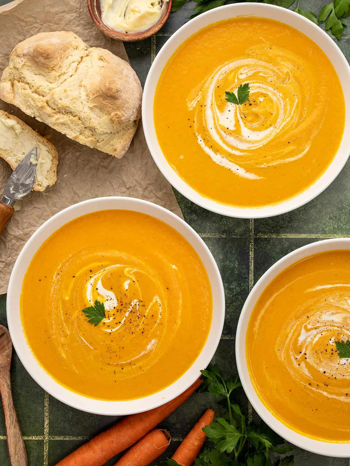 Overhead shot of three bowls of carrot soup with sour cream swirled in them.