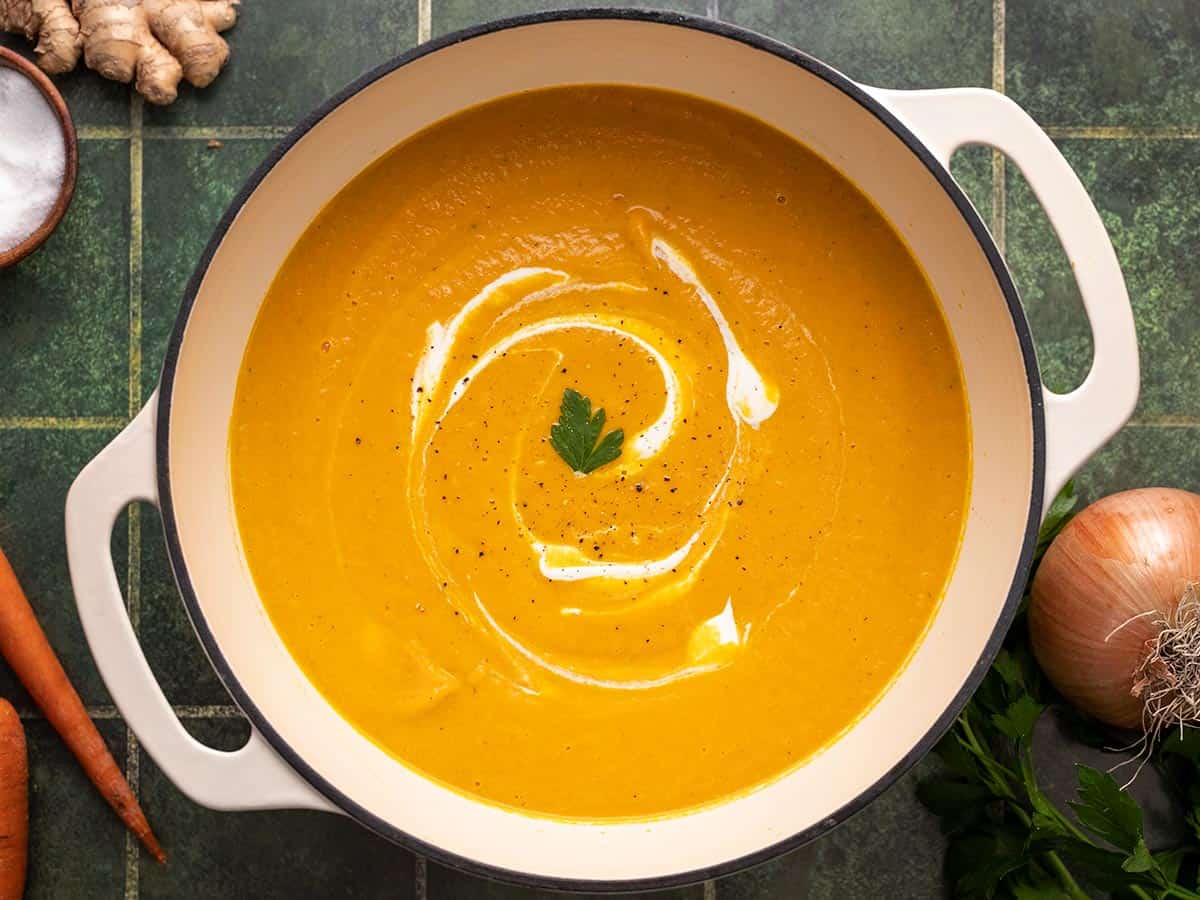 Overhead shot of carrot soup in a white Dutch Oven with sour cream swirled in it.