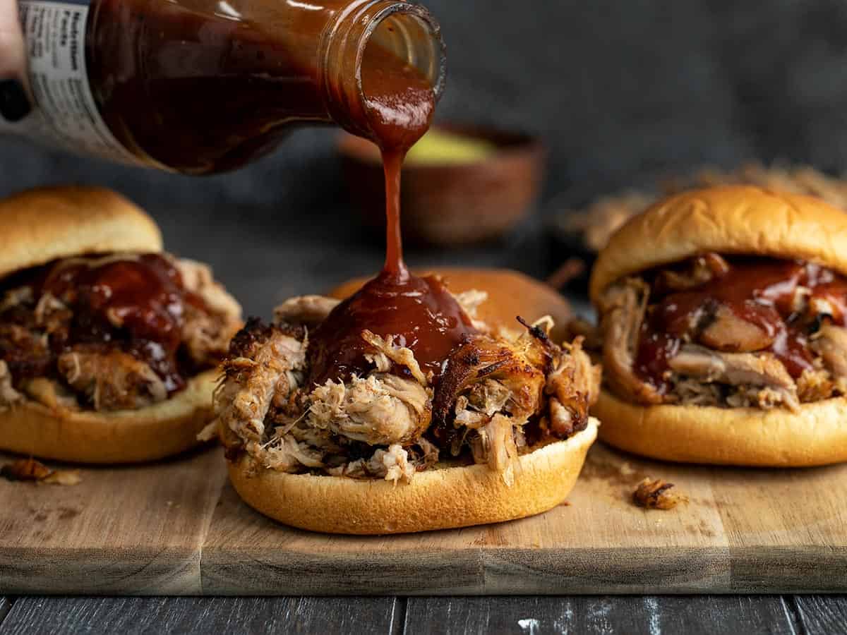 BBQ sauce being poured onto pulled pork sandwiches.