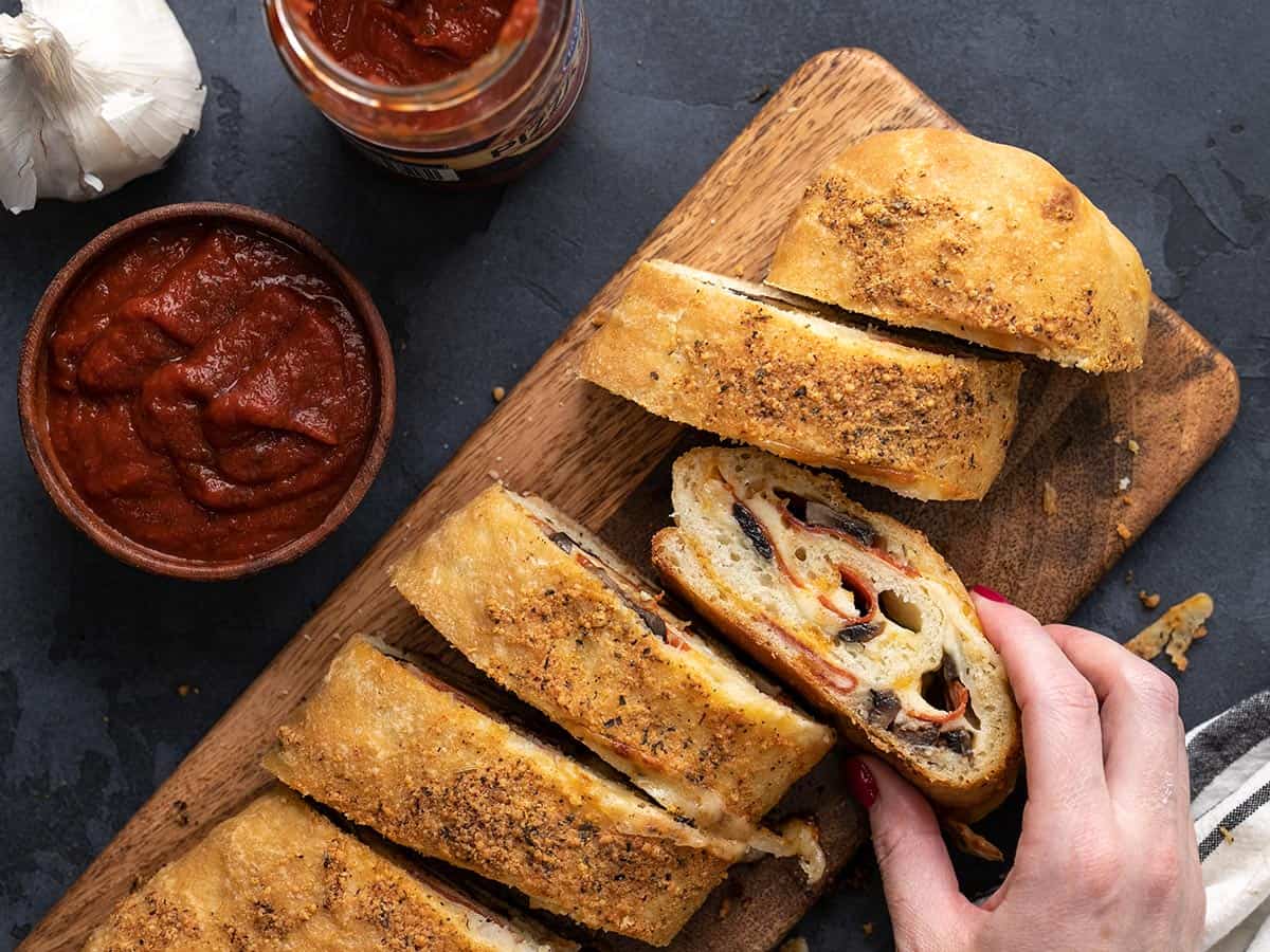 A hand taking one slice of stromboli from the roll.