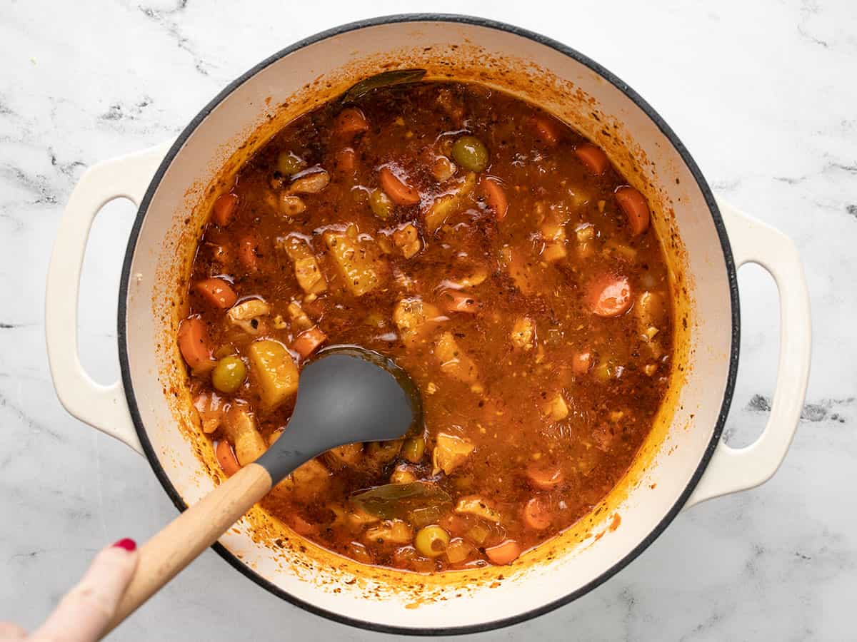 Overhead shot of Guisado de Pollo in a white Dutch oven with a spoon in it.