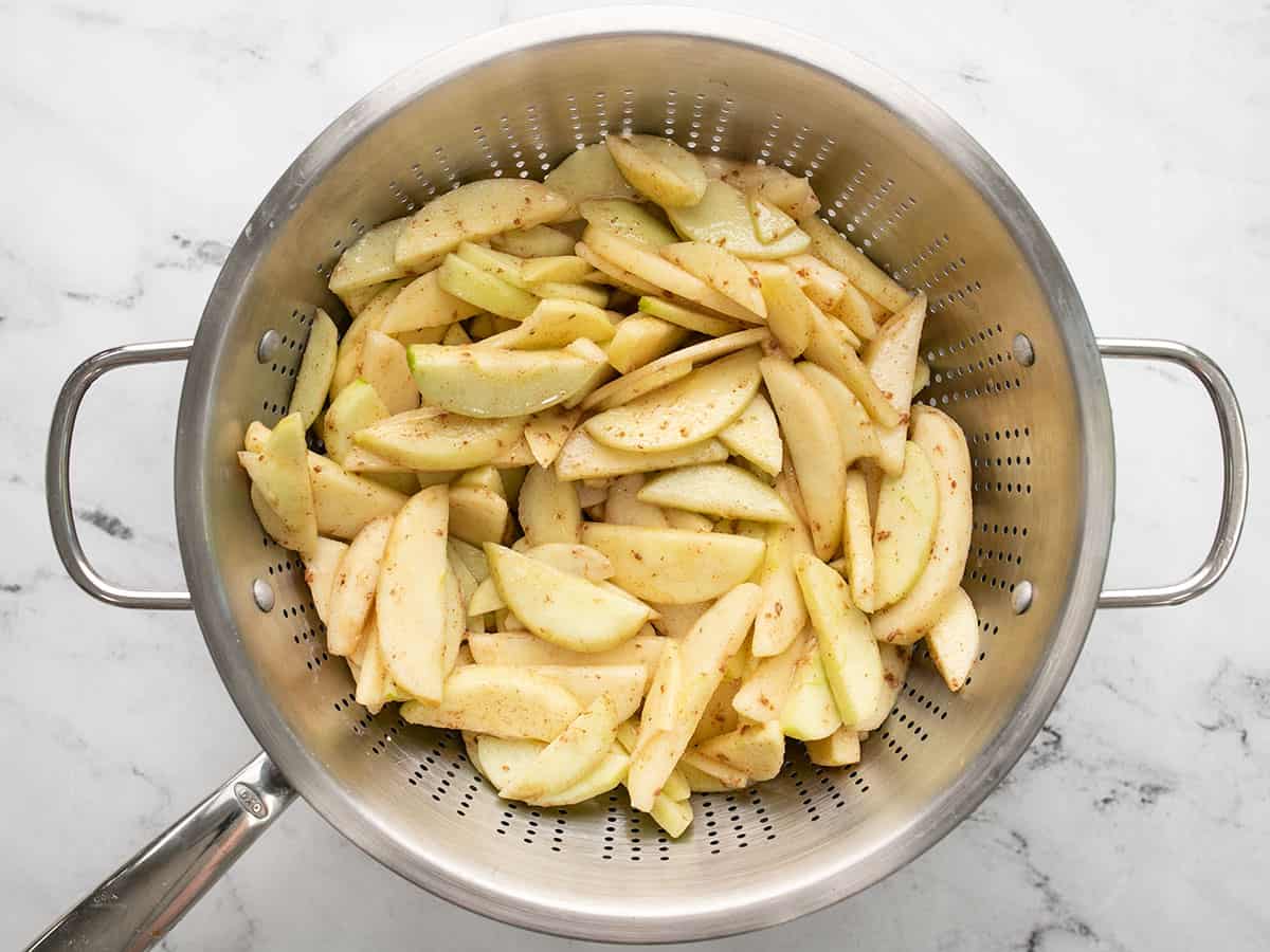 Overhead shot of apples macerating in a colander placed inside a pan.