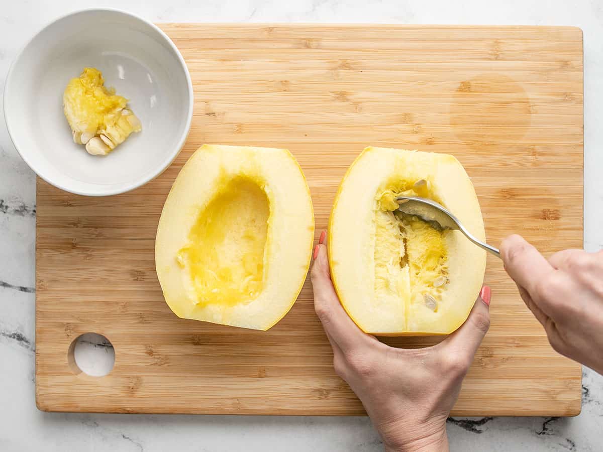 Overhead shot of hands holding a cut squash half and using a spoon to scrape it.