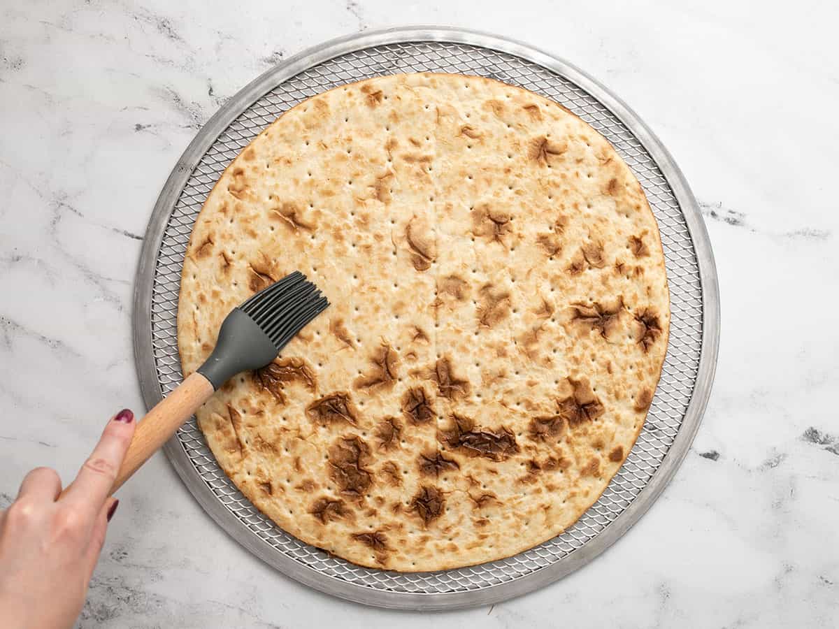 Bacon fat being brushed over the pizza crust.